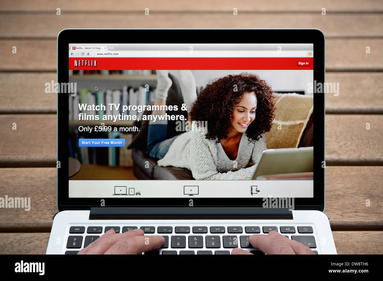 The Netflix website on a MacBook against a wooden bench outdoor background including a man's fingers (Editorial use only). Stock Photo