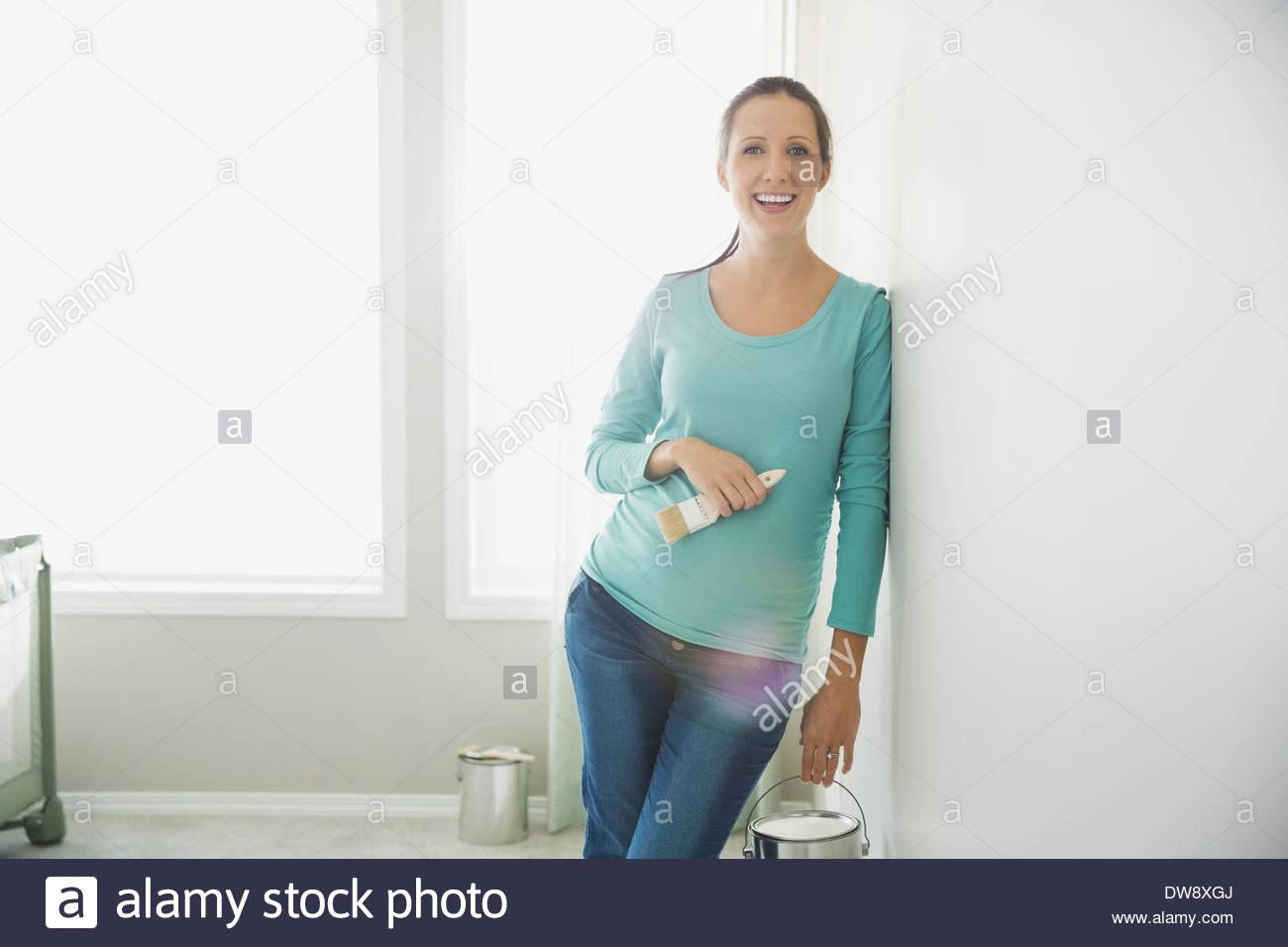 Portrait of pregnant woman with paint can leaning against wall Stock