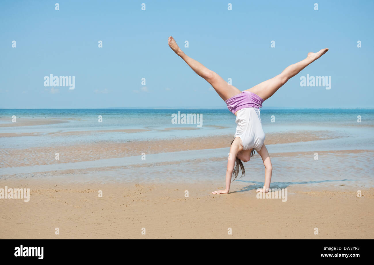 Beautiful energetic young woman doing handstand on the beach Stock Photo