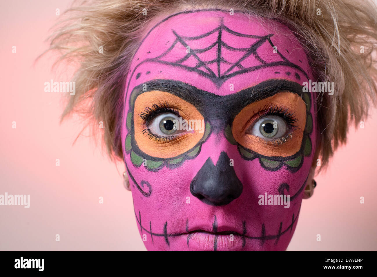 Close-up shot of a young woman with zombie style face paint in pink and wild hair striking a horror pose for the camera. Stock Photo