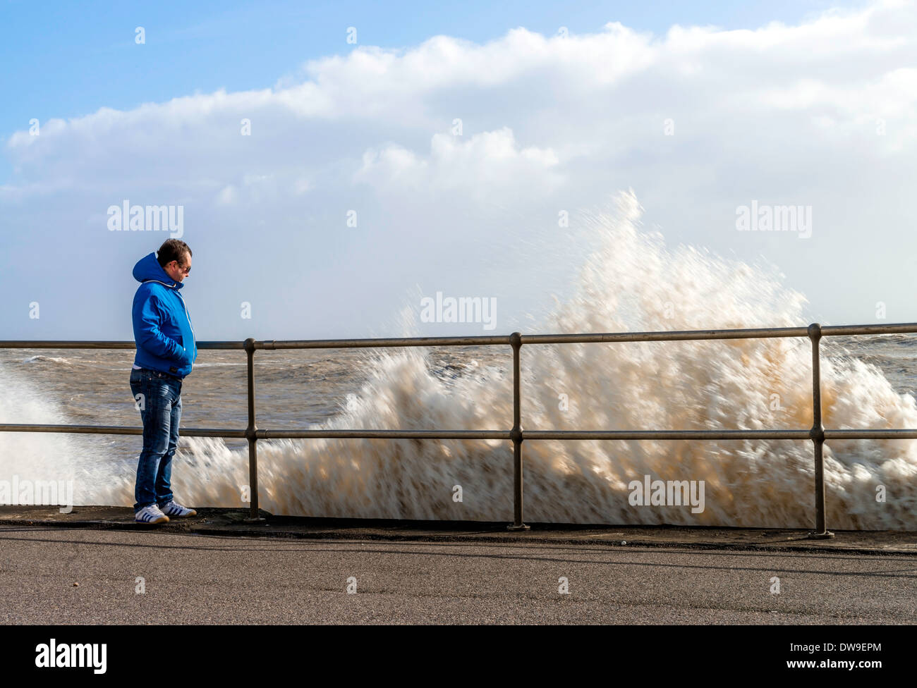 Man leaning on railing alongside of waves breaking, Sussex, UK Stock Photo