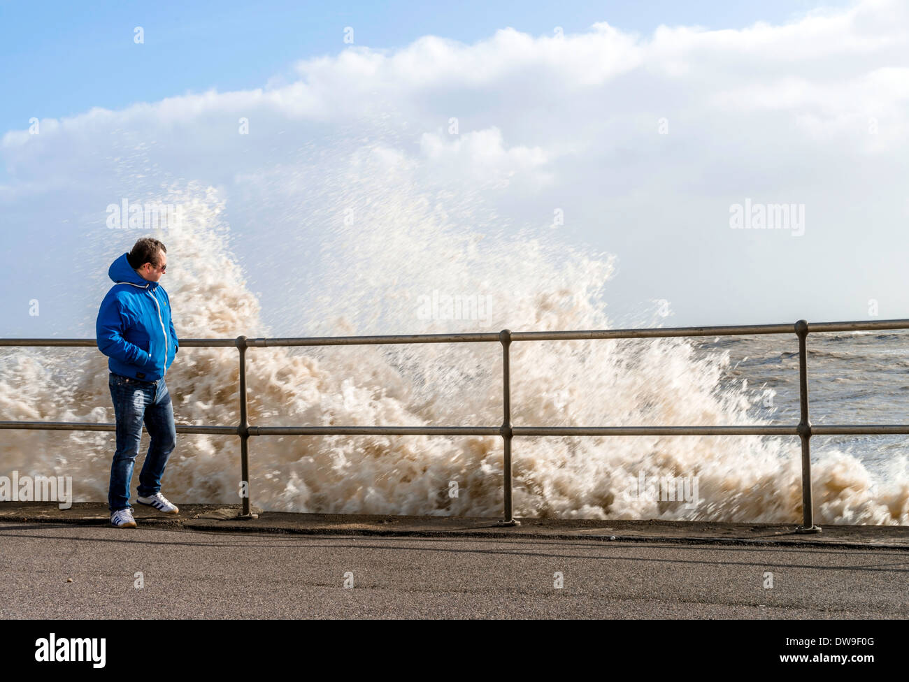 Man leaning on railing alongside of waves breaking, Sussex, UK Stock Photo