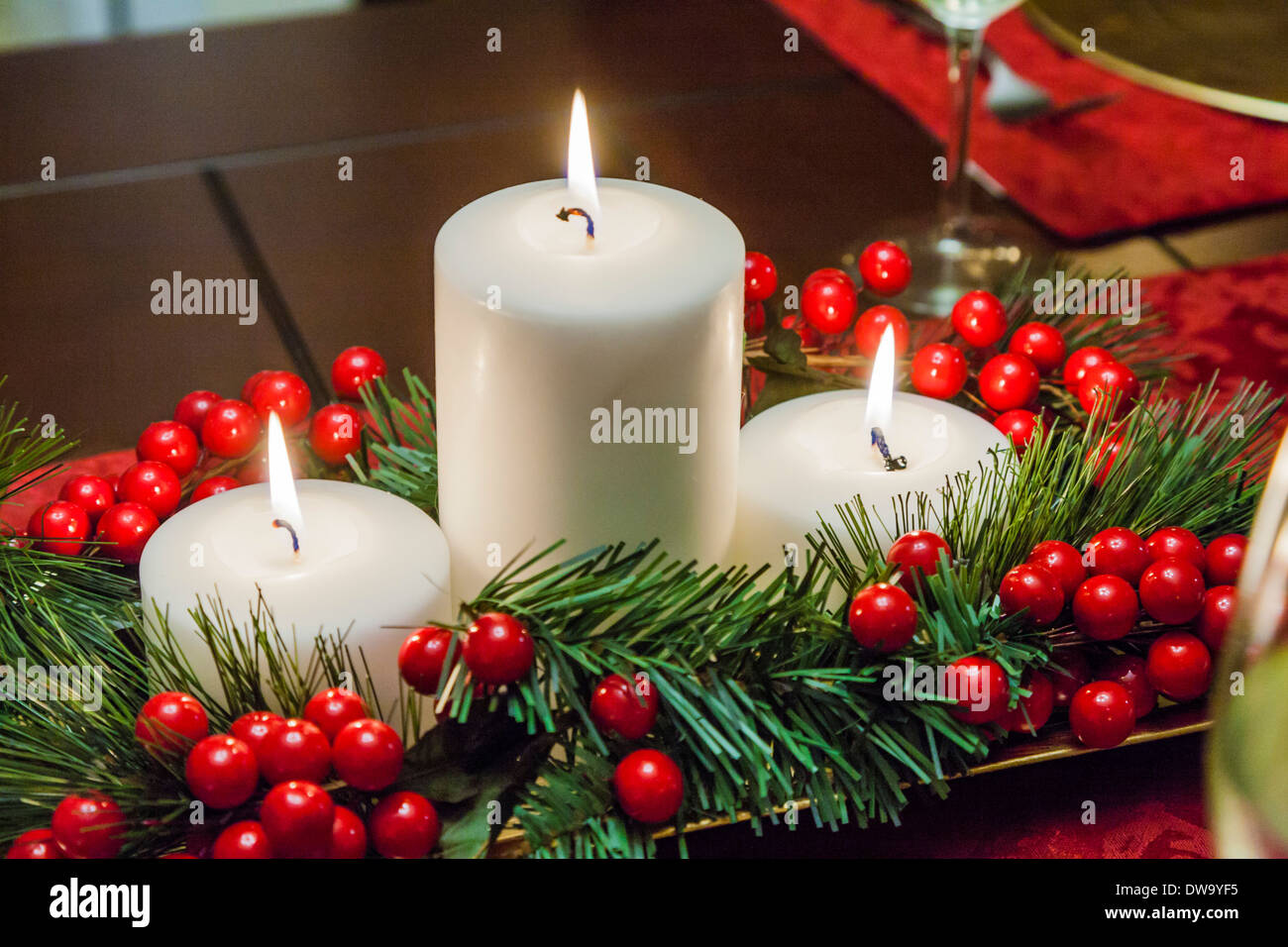 Three tiered candles with garland and holly berries decorate Christmas holiday table Stock Photo
