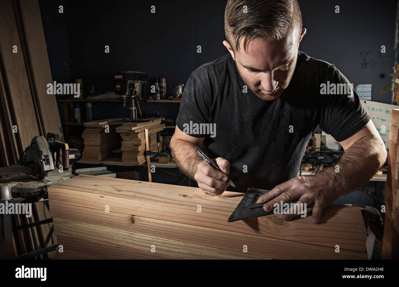 Male carpenter measuring wooden plank with set square in workshop Stock Photo