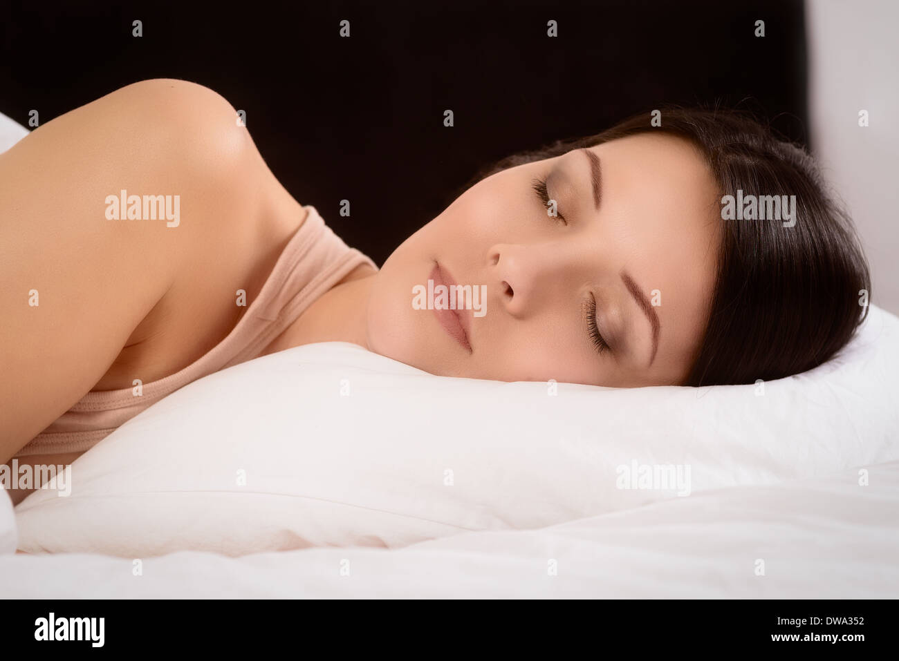 Attractive young woman enjoying a peaceful sleep tucked up in bed dreaming with a serene expression Stock Photo