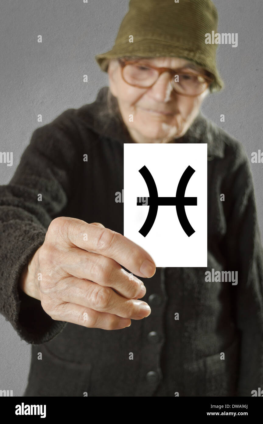 Elderly woman holding card with printed horoscope Pisces sign. Selective focus on card and fingers. Stock Photo