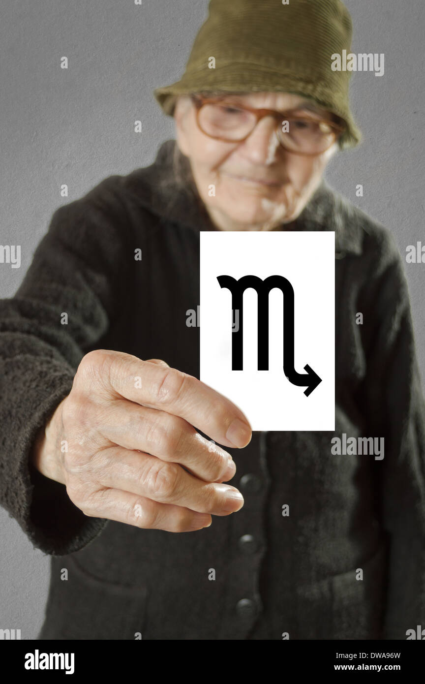 Elderly woman holding card with printed horoscope Scorpio sign. Selective focus on card and fingers. Stock Photo