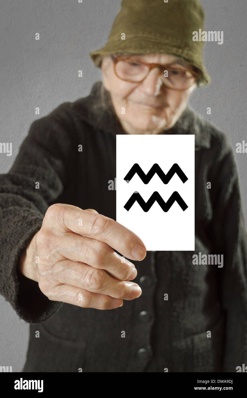 Elderly woman holding card with printed horoscope Aquarius sign. Selective focus on card and fingers. Stock Photo