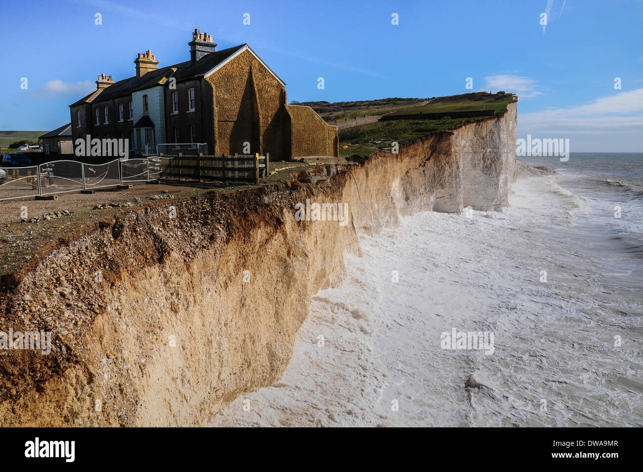 Birling Gap, East Sussex, UK..4 March 2014. High tide on a bright blustery  day as waves continue to erode the cliffs. The end cottage is now being  undercut at the corner. Recent