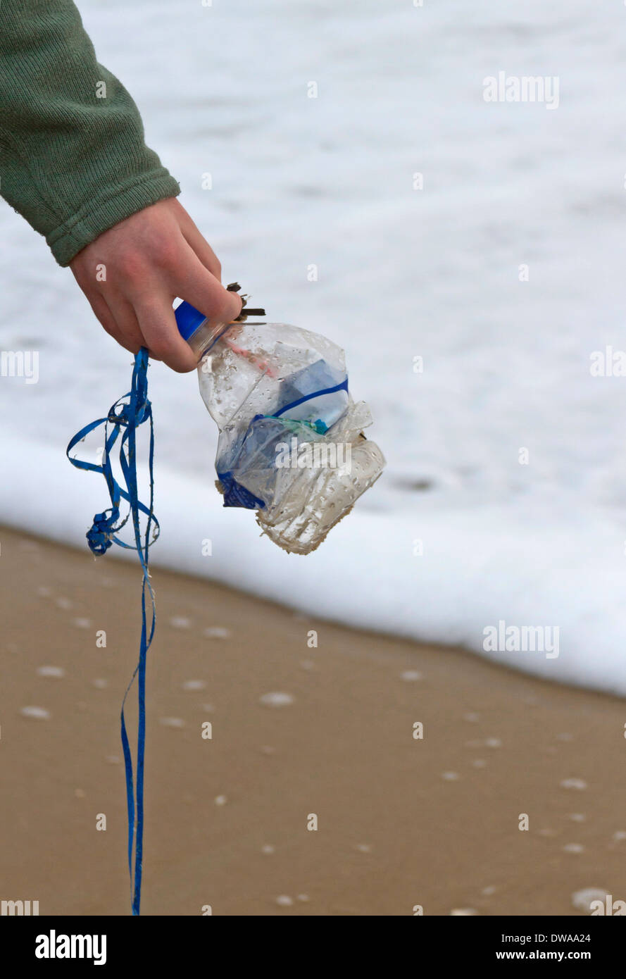 A young womans hand holds a crushed plastic bottle by the sea after picking it up off the beach Stock Photo