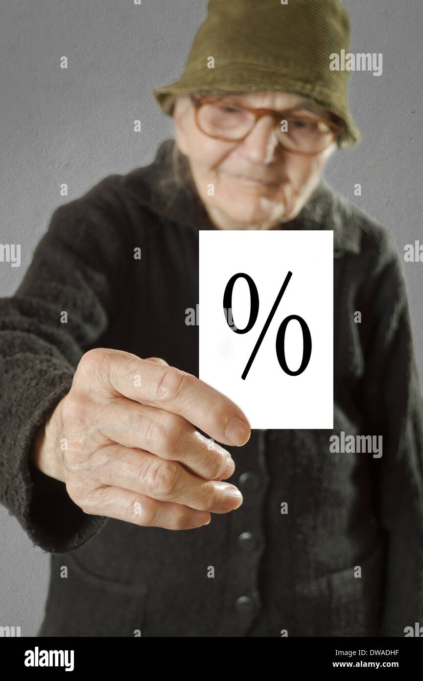 Elderly woman holding card with printed percent sign. Selective focus on card and fingers. Stock Photo