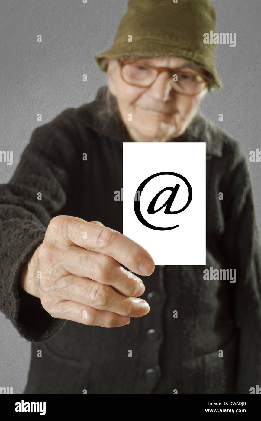 Elderly woman holding card with printed e-mail sign. Selective focus on card and fingers. Stock Photo