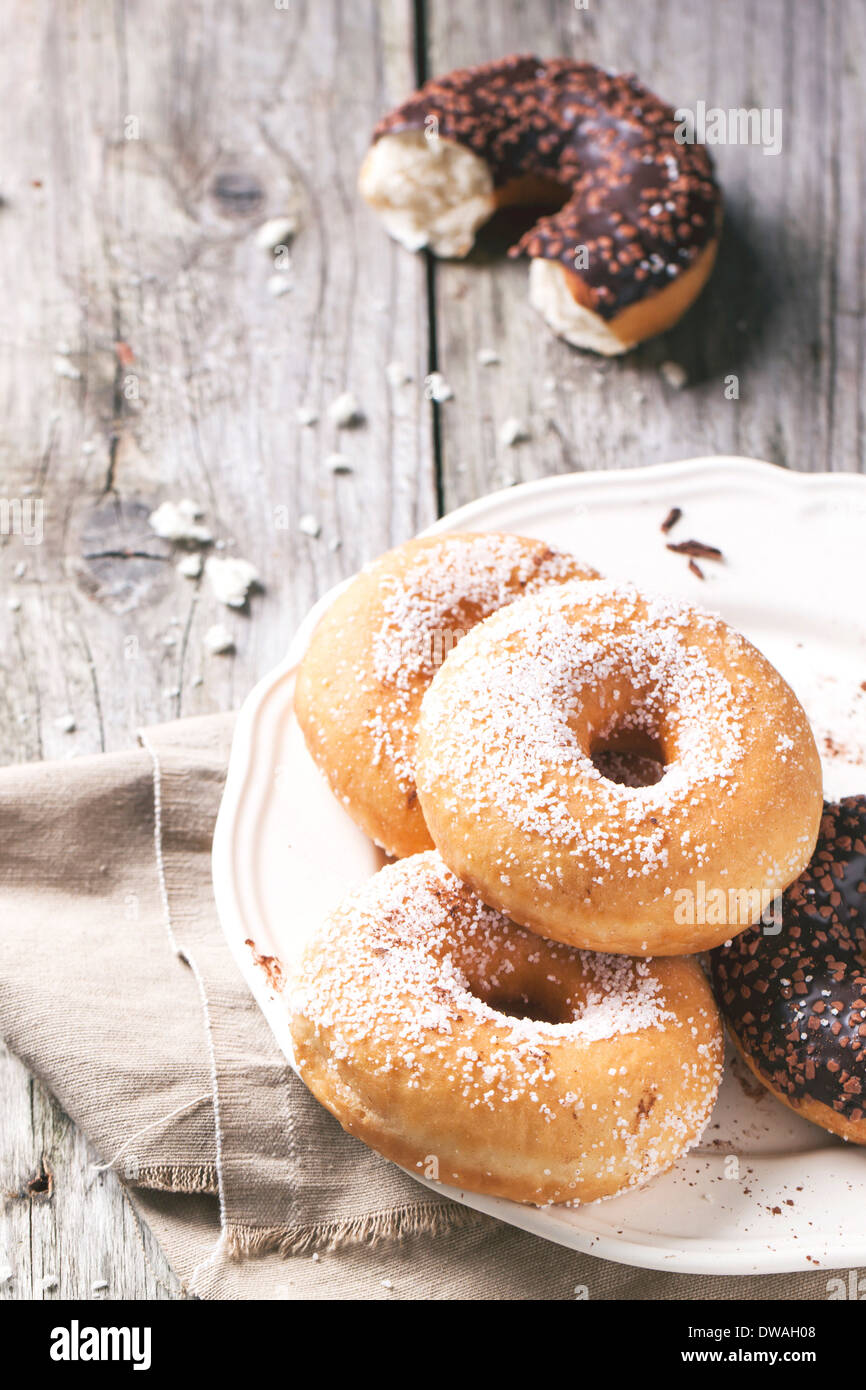 White plate of sugar donuts and half of chocolate donut served on wooden table. Stock Photo
