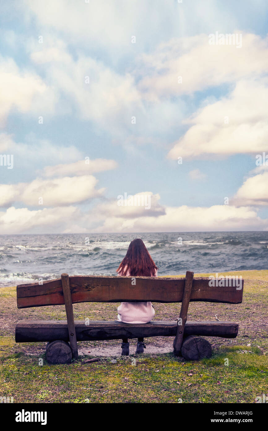 a woman is sitting on a bench at the sea Stock Photo