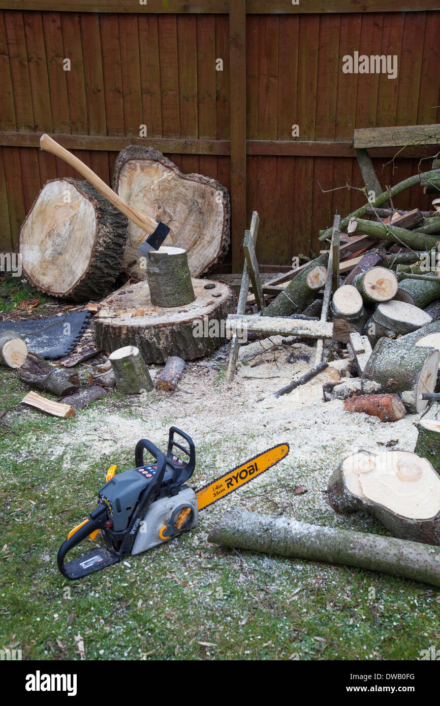 An axe in a piece of wood on a chopping block and a chain saw for Stock