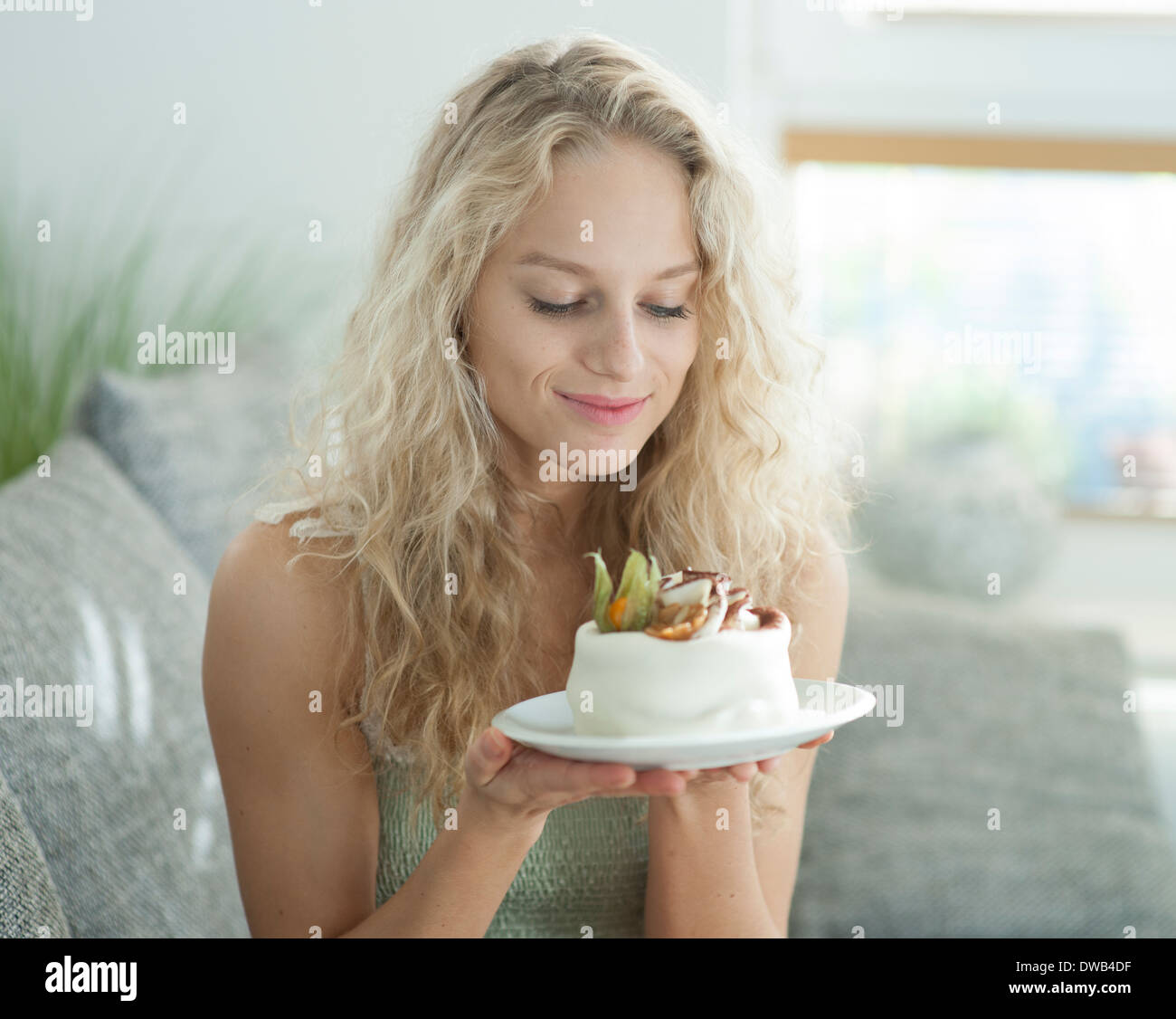 Beautiful young woman looking at tempting cake in house Stock Photo