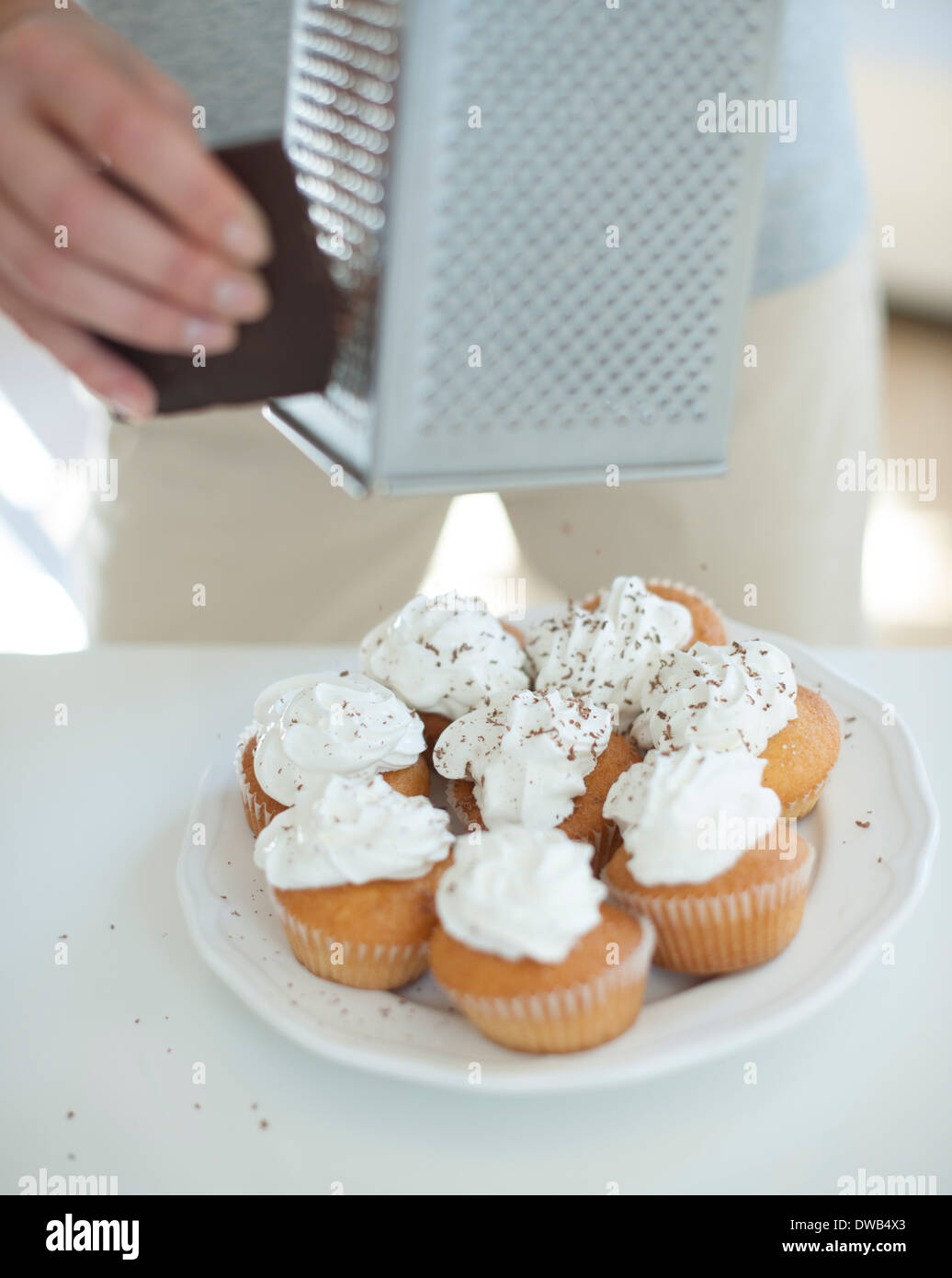 Cropped image of woman grating chocolate on cupcakes at counter Stock Photo
