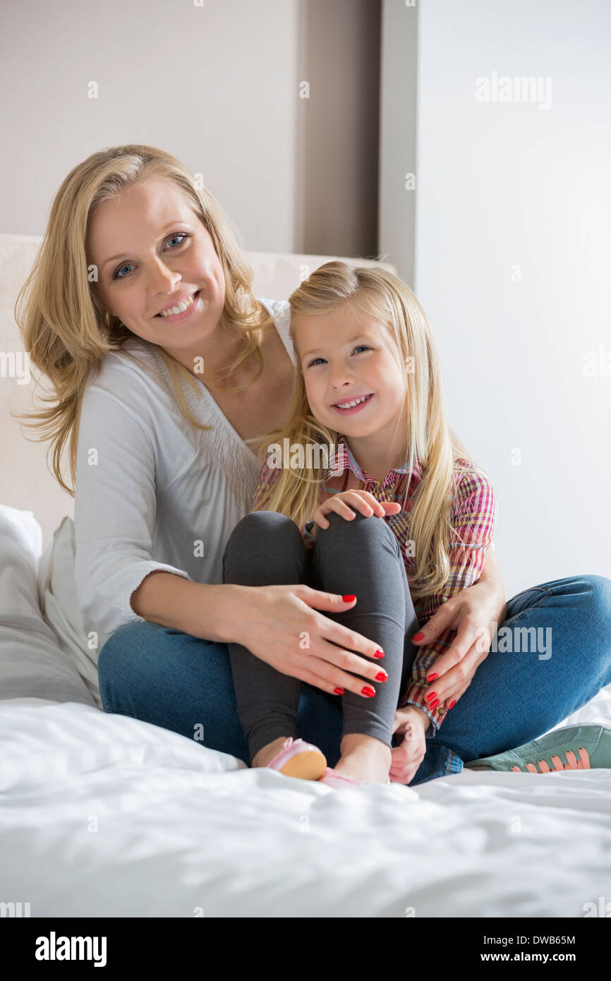 Portrait of happy mother and daughter sitting on bed at home Stock Photo