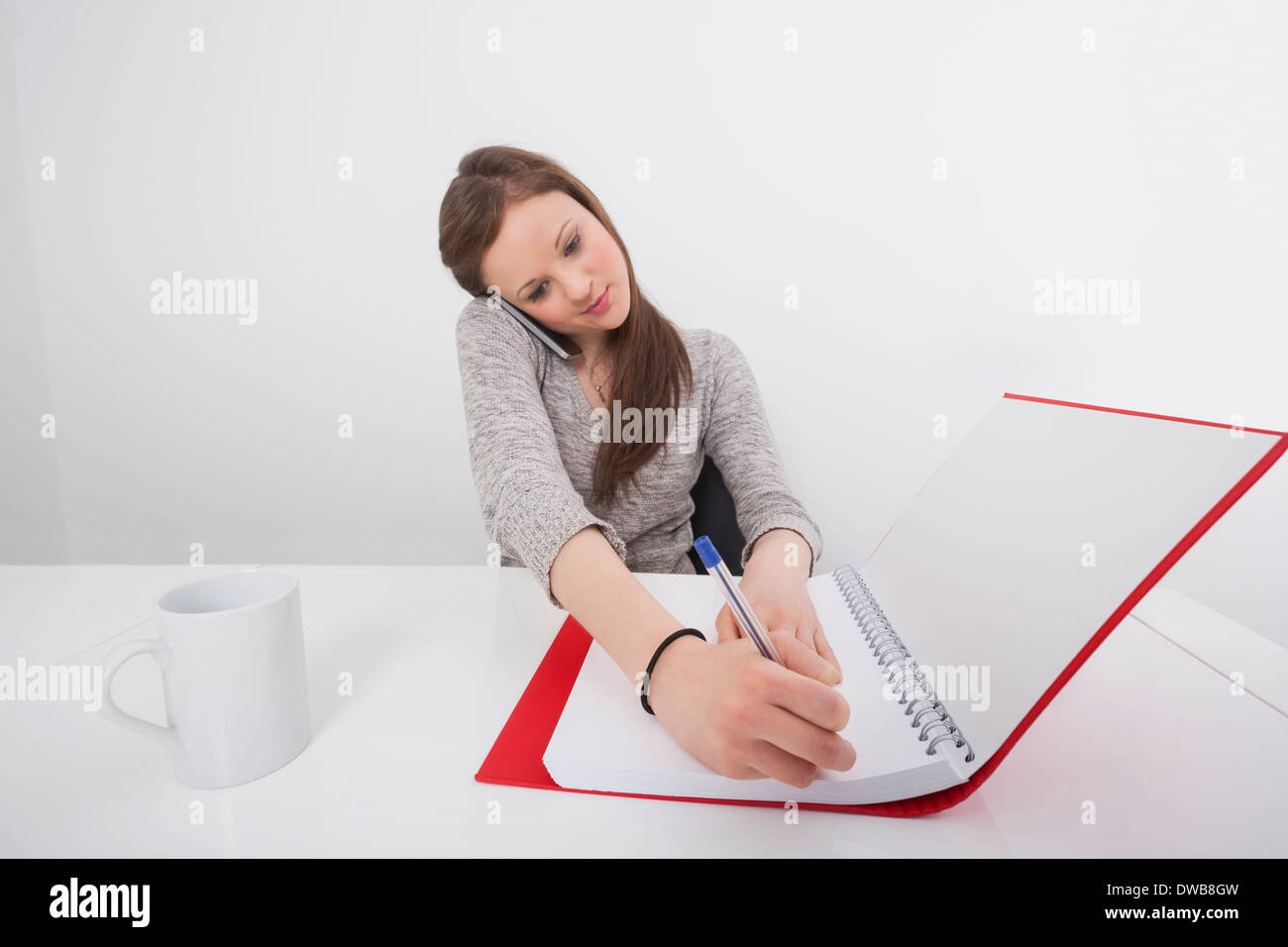 Businesswoman writing notes while answering smart phone in office Stock Photo