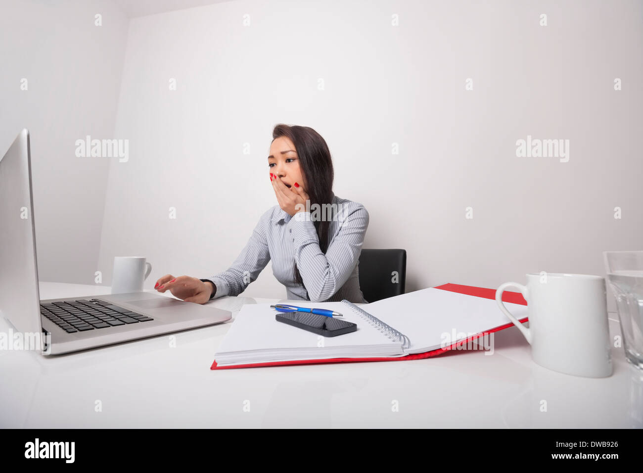 Sleepy businesswoman working on laptop at office desk Stock Photo