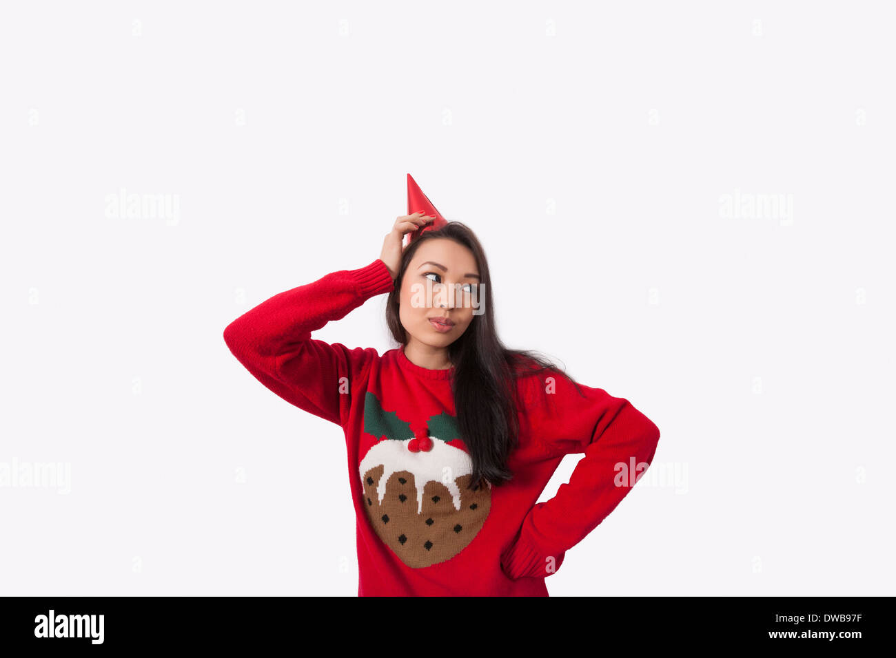 Woman wearing Christmas jumper and party hat against gray background Stock Photo