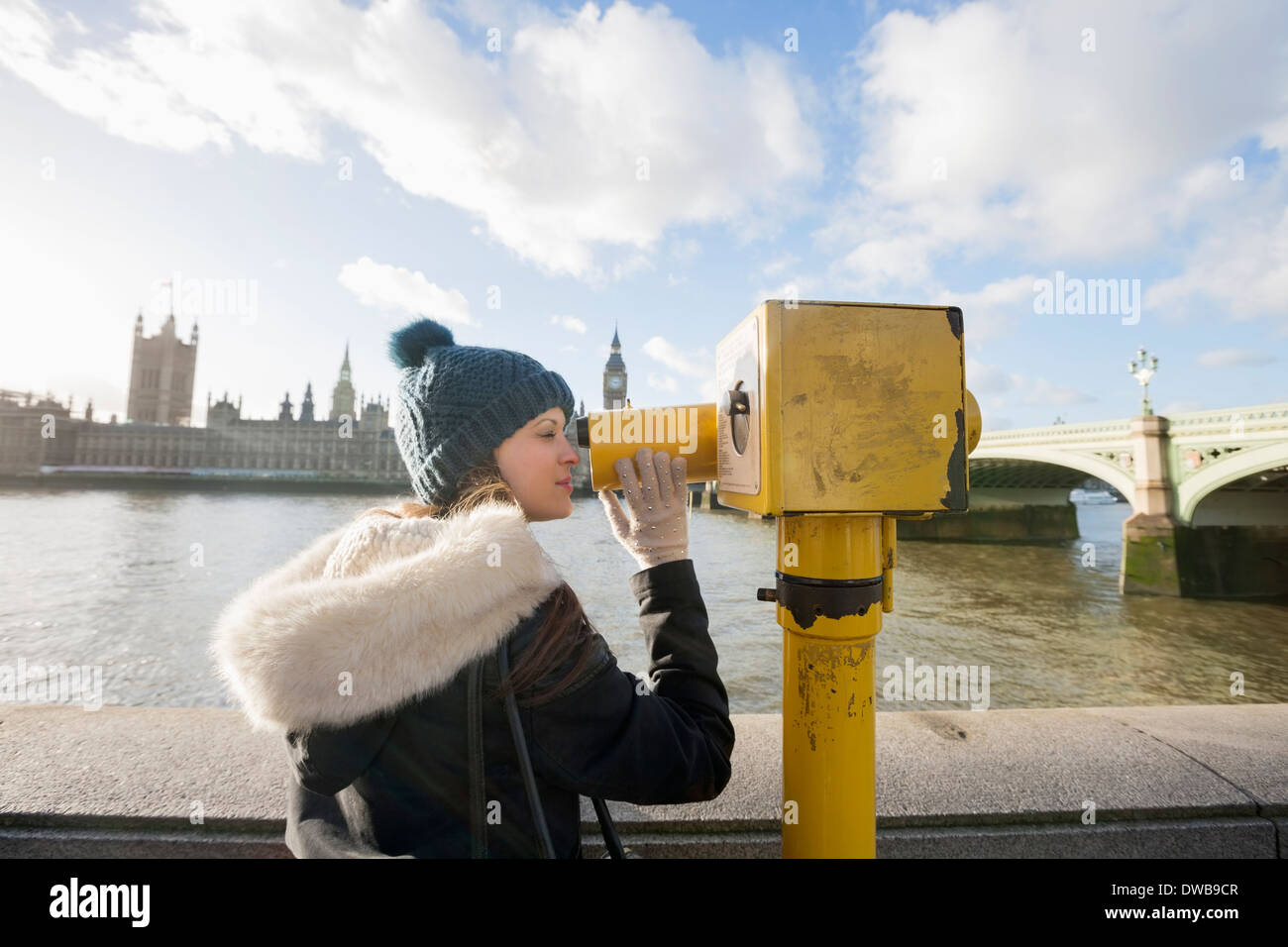 Side view of young woman looking through telescope by river Thames, London, UK Stock Photo