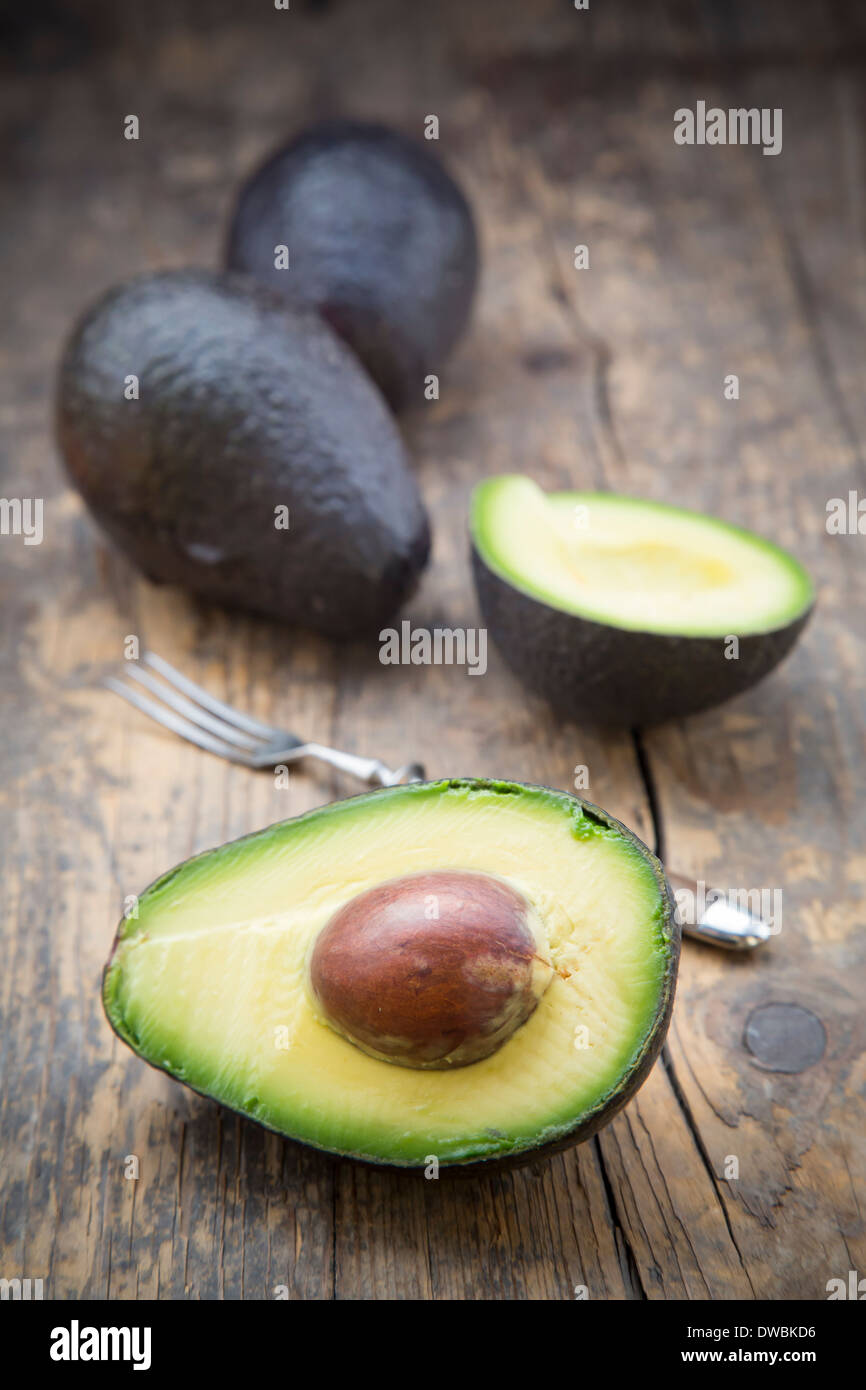 Sliced and whole avocados (Persea Americana) on wooden table Stock ...
