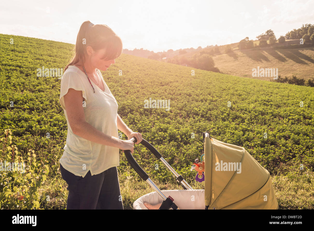 Mother strolling in countryside pushing baby pram Stock Photo