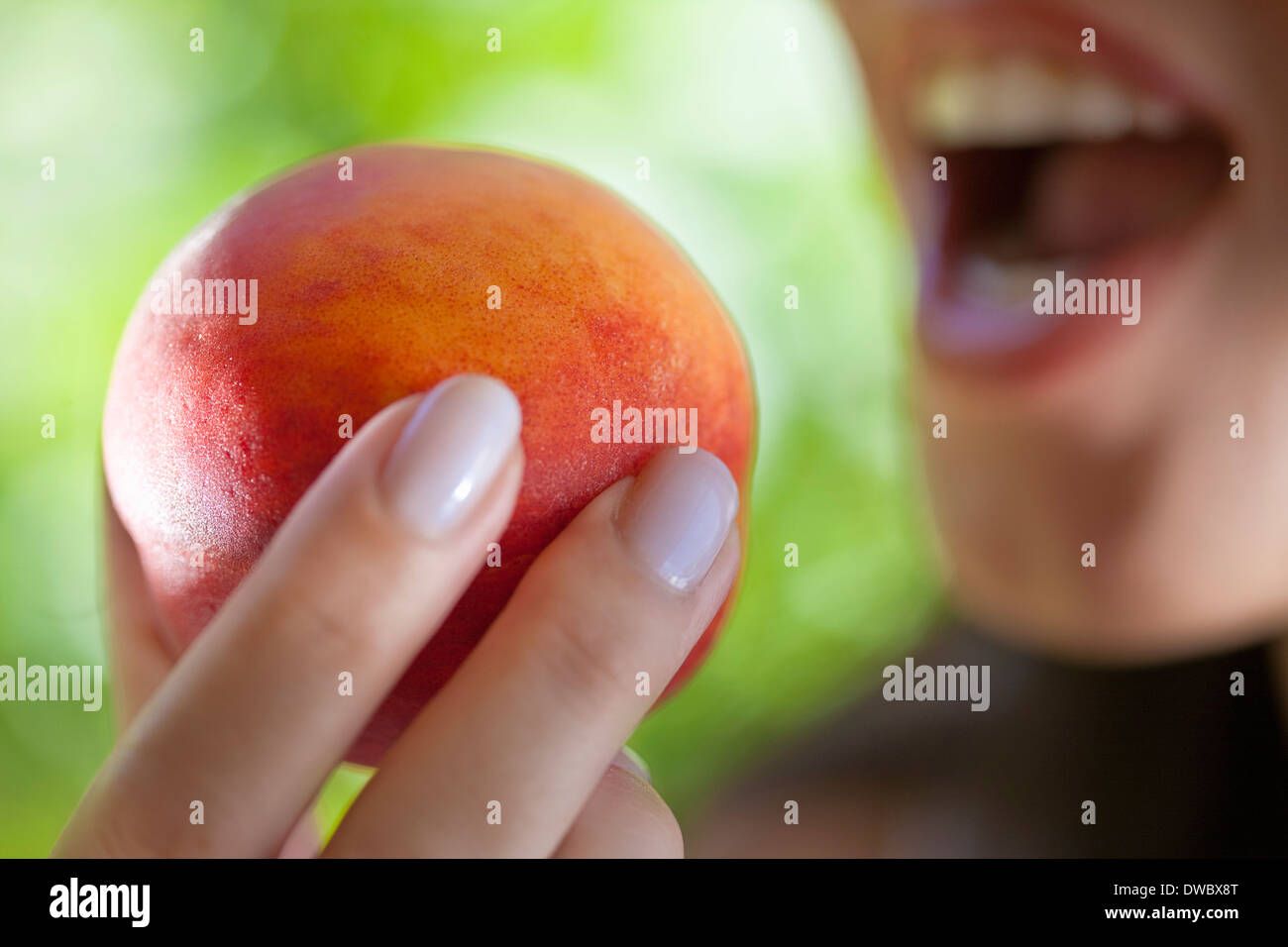 Woman holding peach to mouth Stock Photo