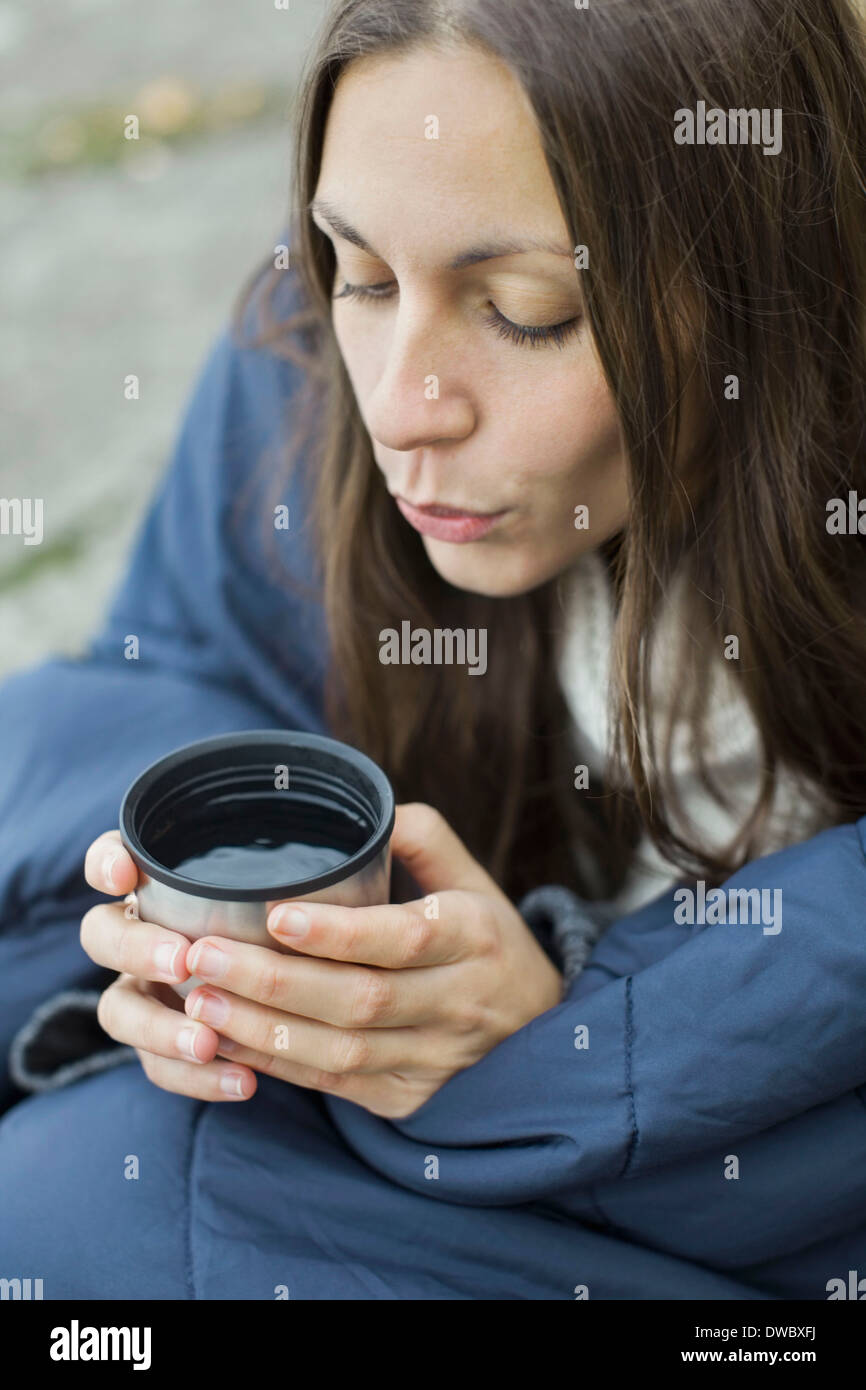 Woman wrapped in blanket blowing on coffee Stock Photo