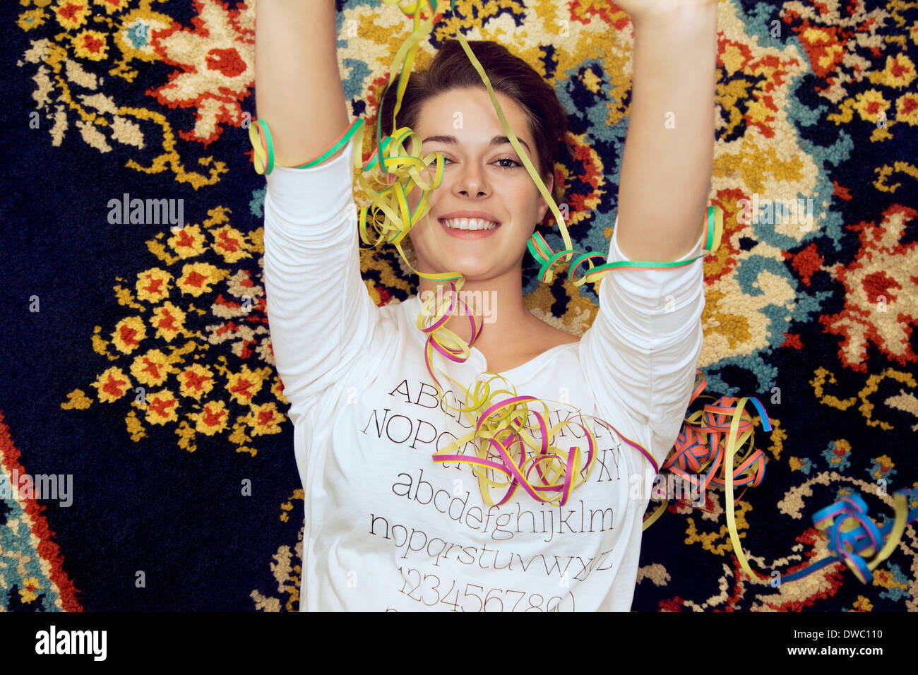 Portrait of young woman and streamers lying on patterned rug Stock Photo