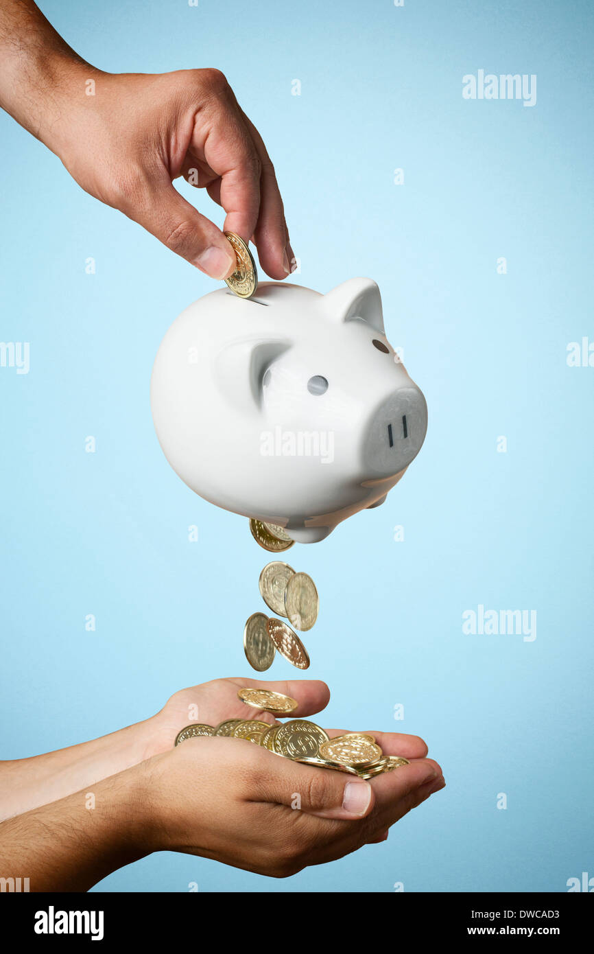 Hand putting coin into piggy bank and coins flowing out Stock Photo - Alamy