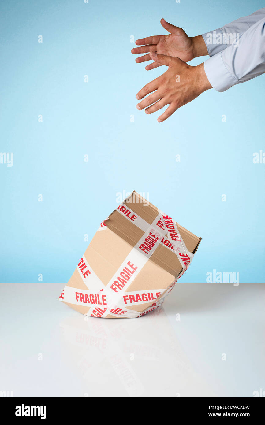 Studio shot of hands dropping cardboard box marked fragile Stock Photo