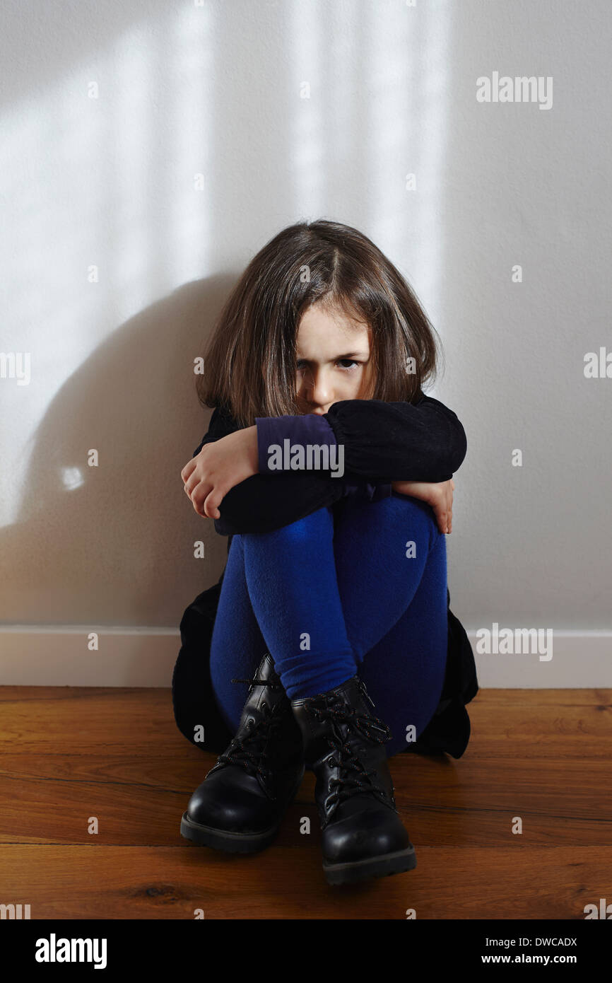 Portrait of stubborn young girl sitting on floor hugging knees Stock Photo