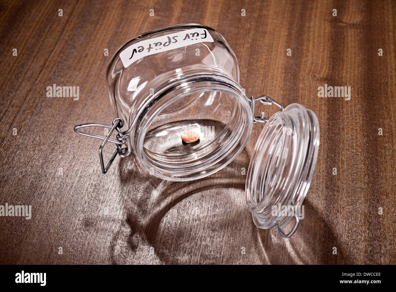 Opened glass jar with the german inscription 'für später' lies opened on a table. The content consists of one cent coin. Stock Photo