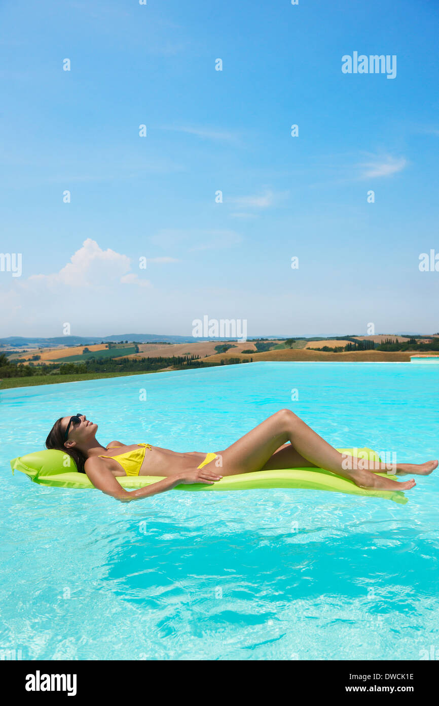 Mid adult woman lying on inflatable mattress in swimming pool Stock Photo