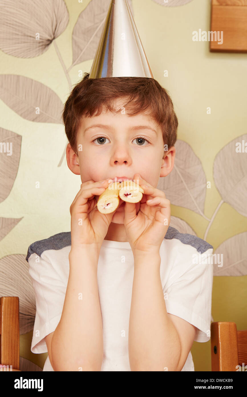 Boy wearing party hat with party food in mouth Stock Photo