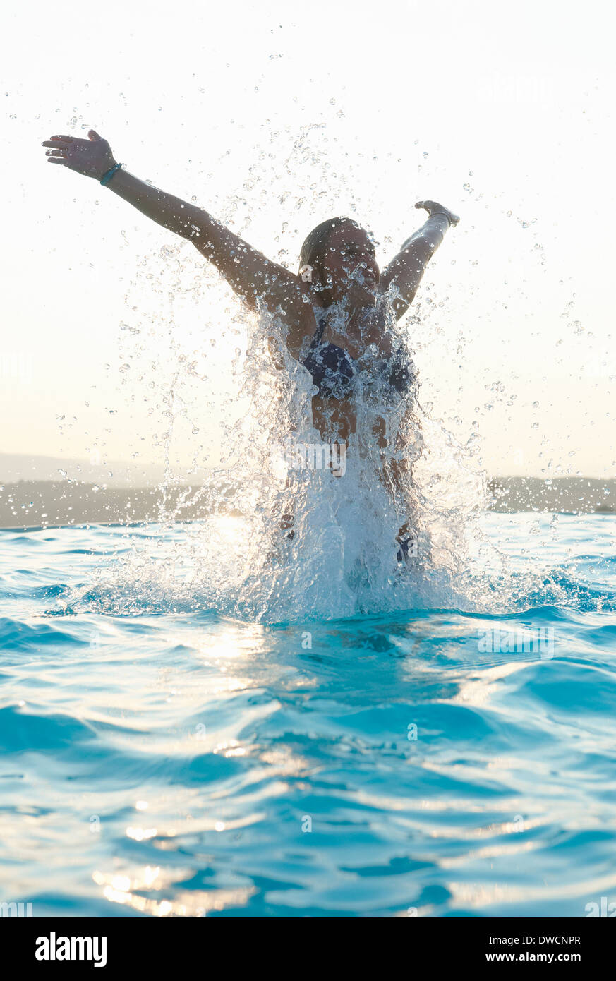 Young woman with arms out splashing in swimming pool Stock Photo