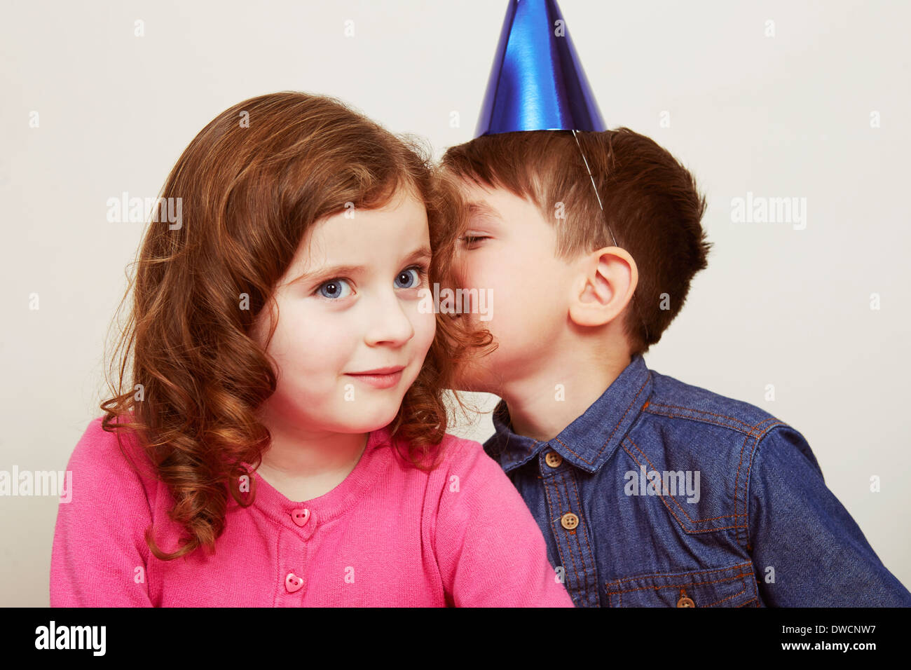 Boy wearing party hat whispering to girl Stock Photo