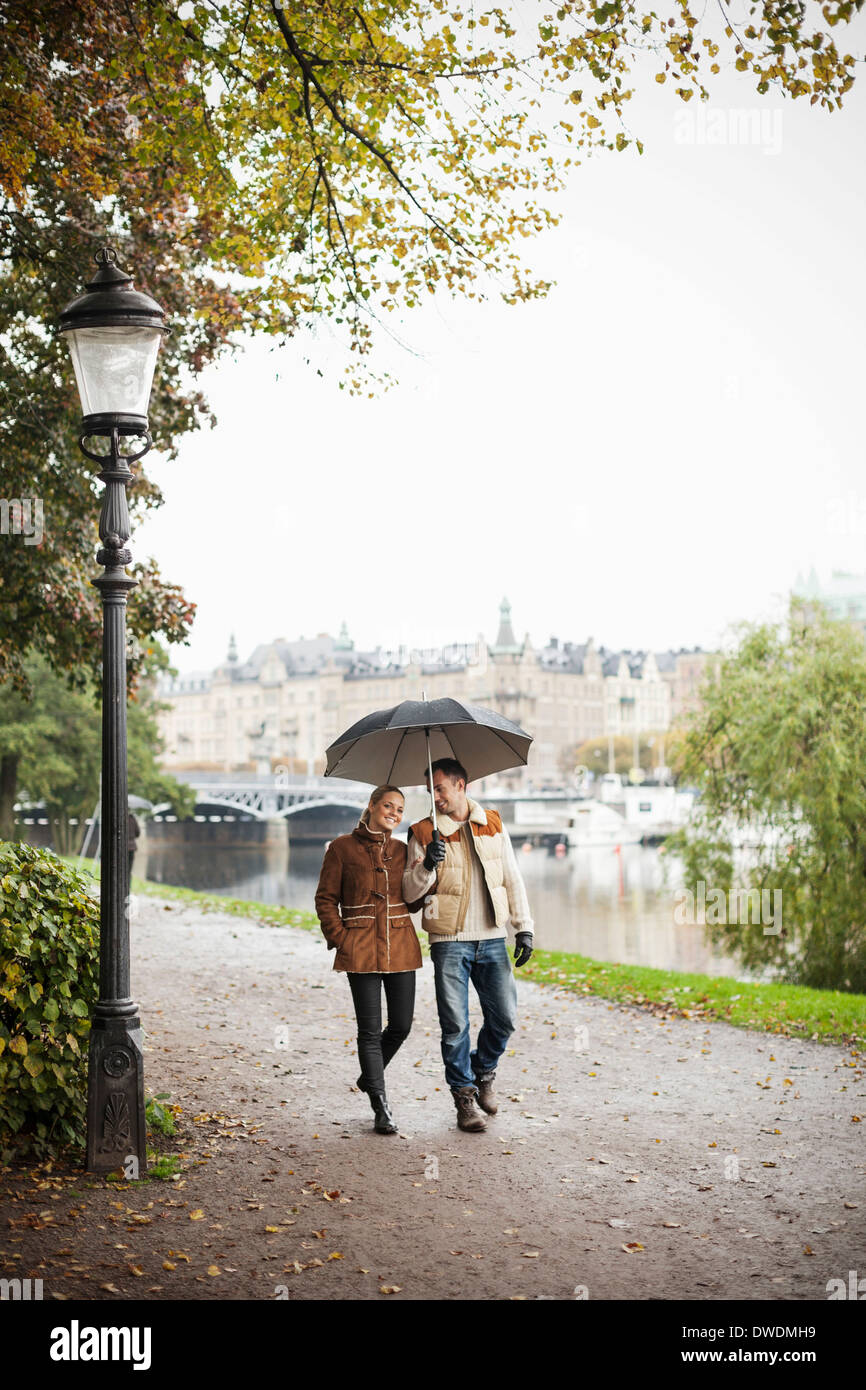 Young couple with umbrella walking on street during autumn Stock Photo