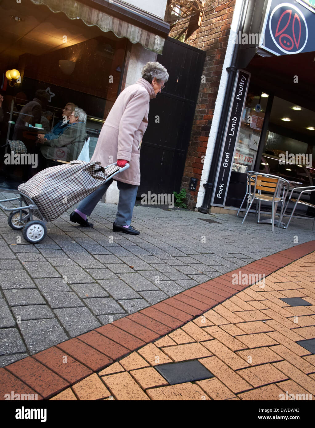 An elderly senior woman pulling a shopping trolley on a uk high street