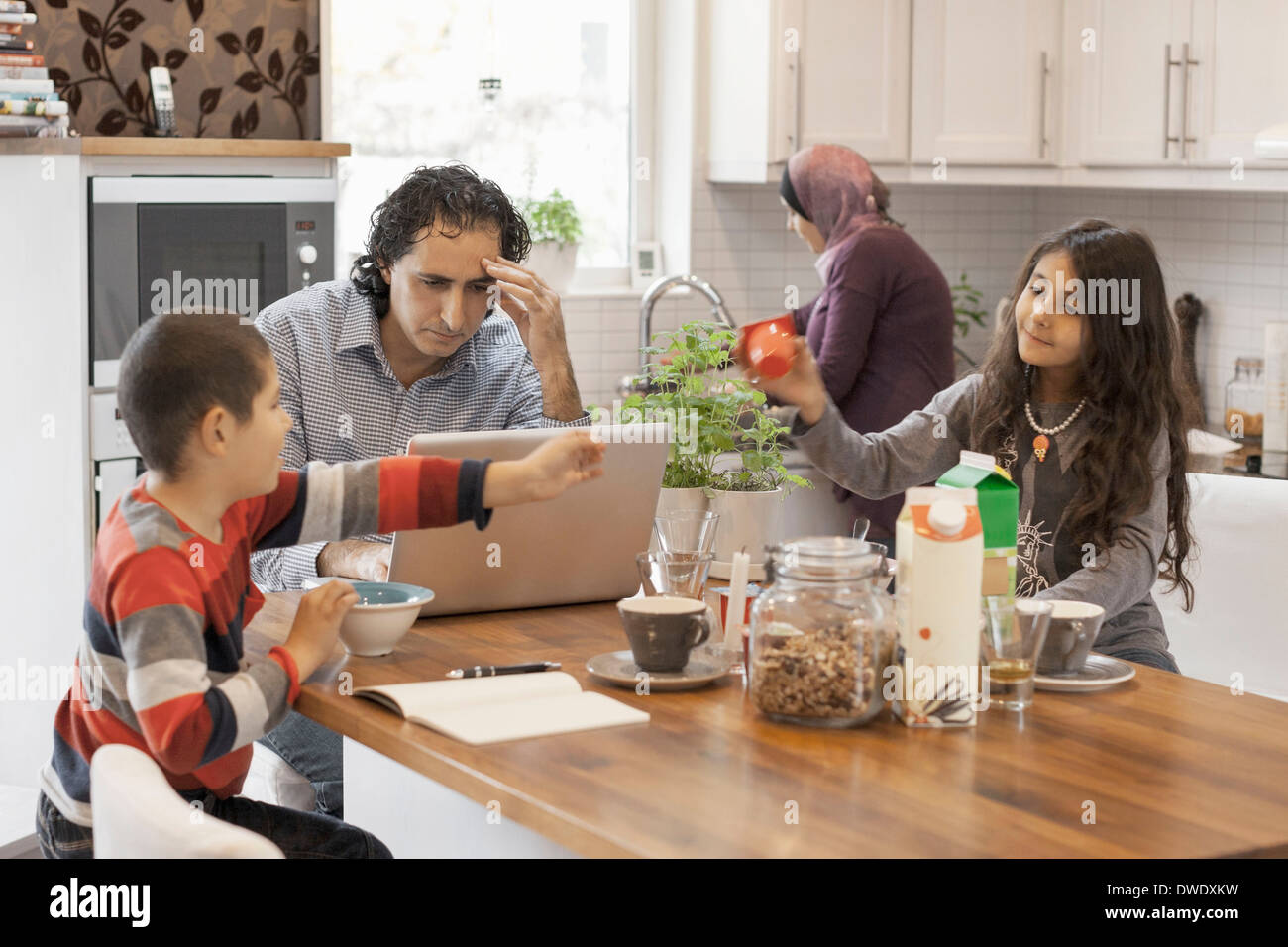 Muslim Man Working On Laptop In Kitchen With Family Having Breakfast Stock Photo Alamy