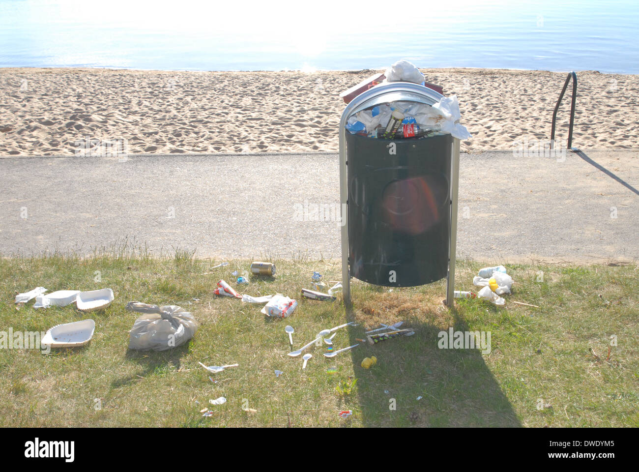 Beach view with full rubbish bin and rubbish covering the ground. Stock Photo