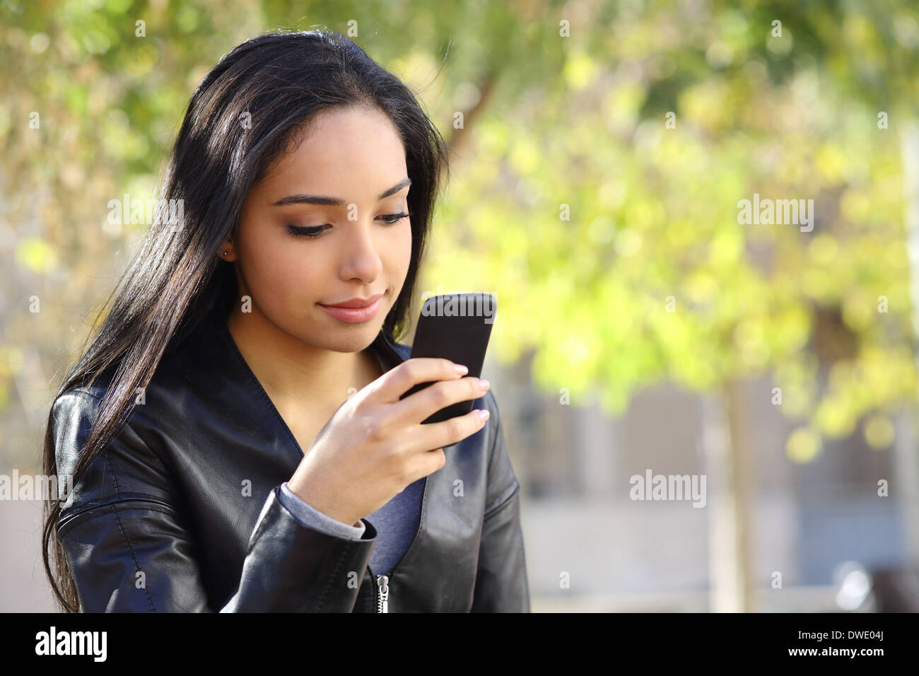 Beautiful woman texting on a smart phone in a park with a green background Stock Photo