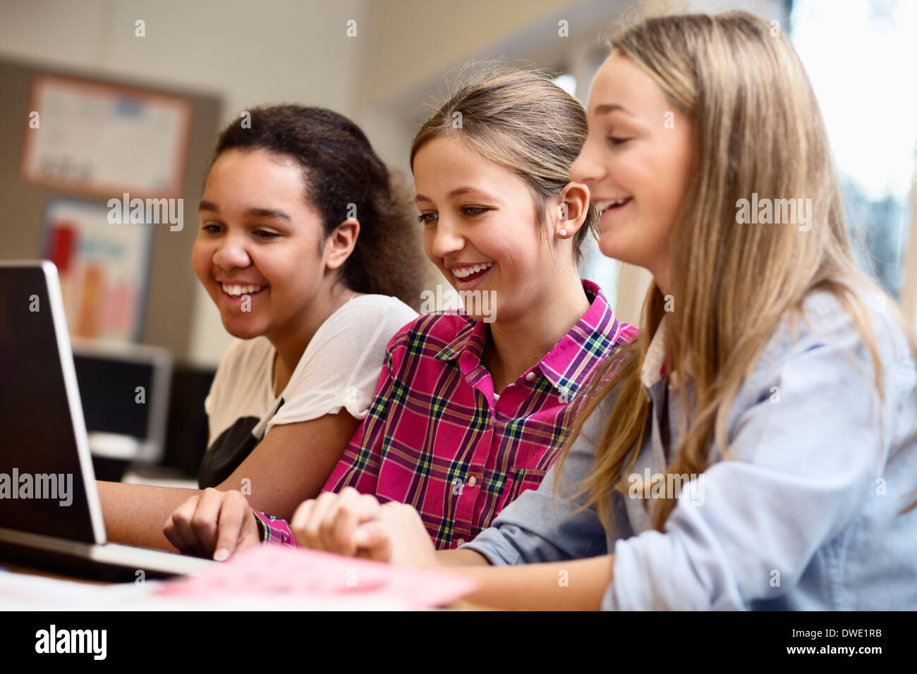 Happy schoolgirls using laptop together in classroom Stock Photo