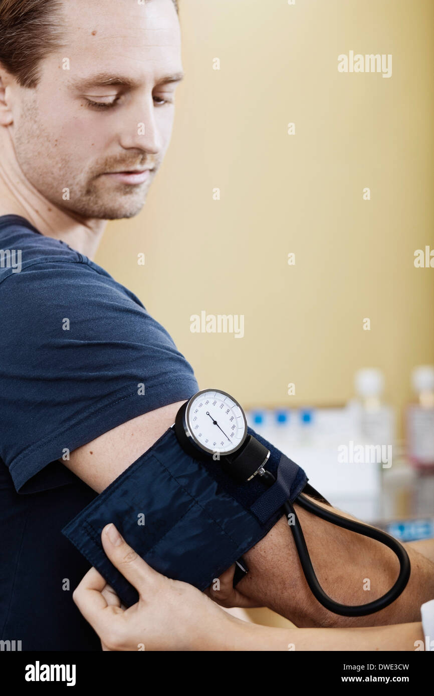 Doctor putting blood pressure cuff on male patient's arm in clinic