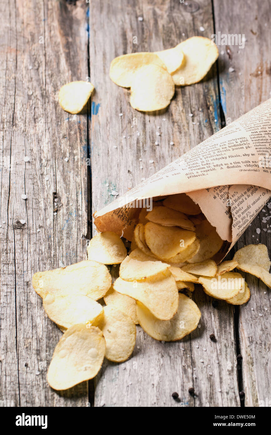 Paper with potato chips with salt and pepper over old wooden