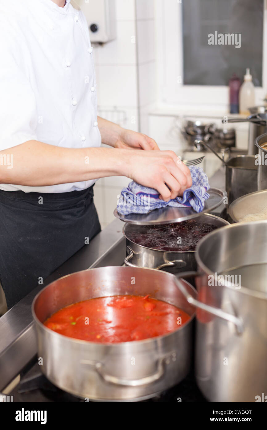 Cooking in a commercial kitchen with large stainless steel pots filled with stew and vegetables on a central gas hob Stock Photo