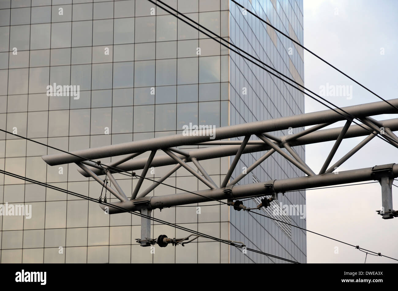 Overhead catenary at Brussels Midi railway station with steel and glass office block behind. Stock Photo