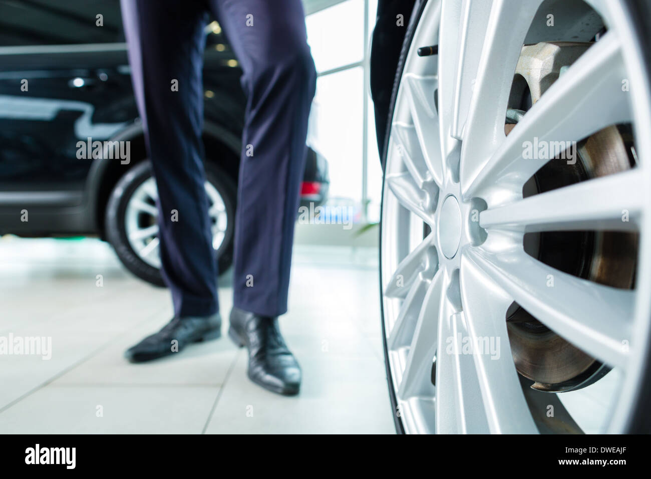 Seller or car salesman in car dealership presenting the extra decorations like sport rims of his new and used cars Stock Photo